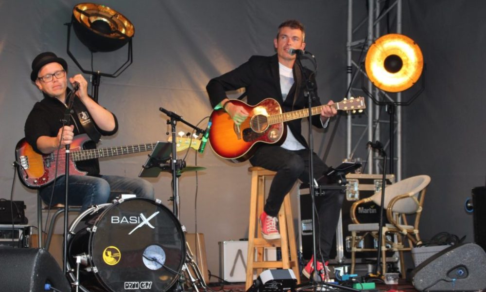 Mads Vejen spillende i band med guitar og trommer på scene